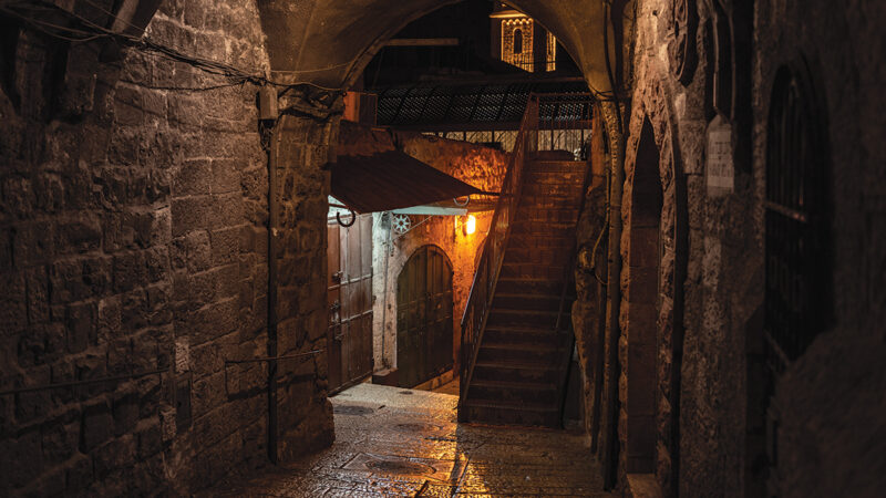 Dimly lit ancient stone alleyway with stairs and archway, creating a mysterious, historic atmosphere at night.