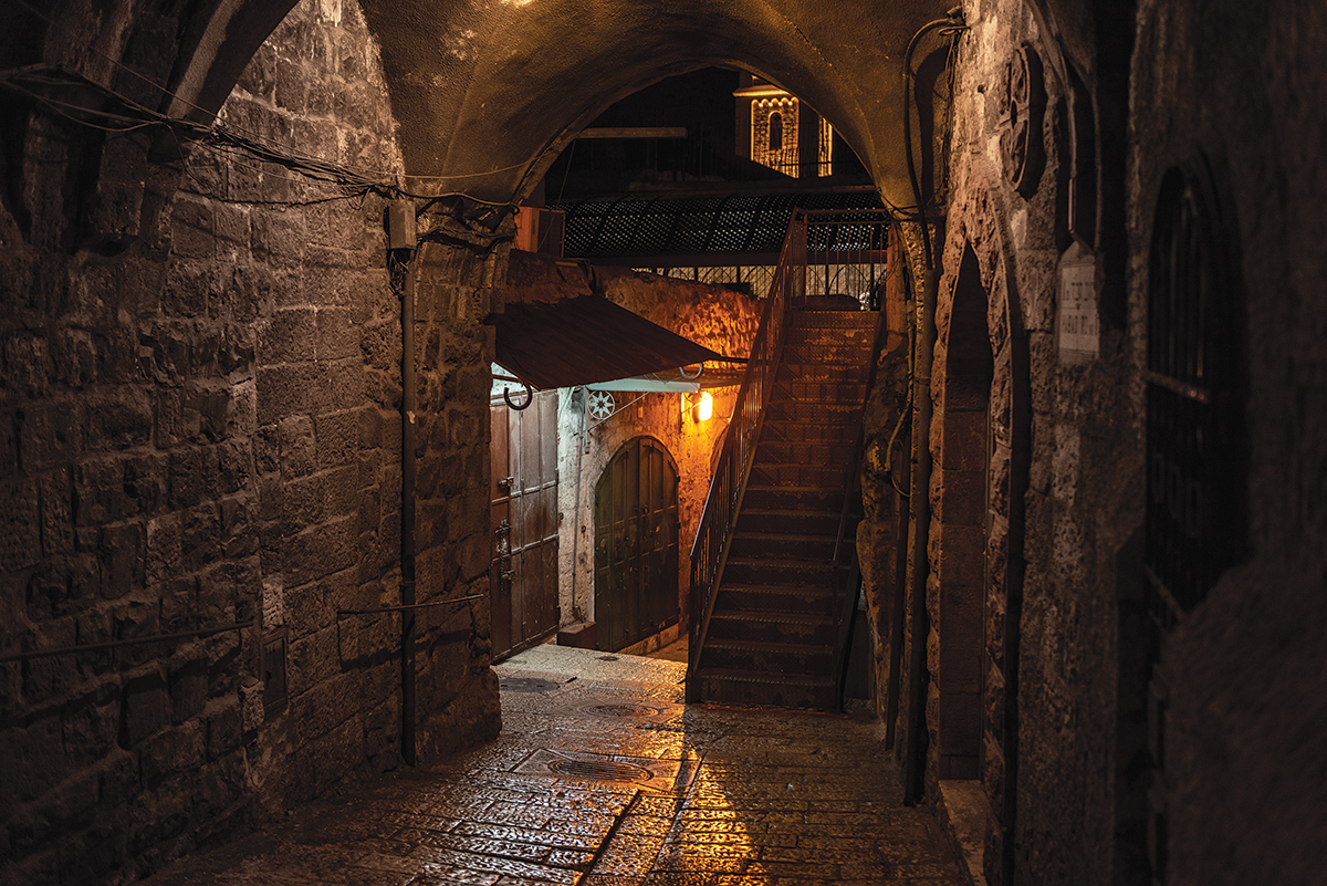 Dimly lit ancient stone alleyway with stairs and archway, creating a mysterious, historic atmosphere at night.