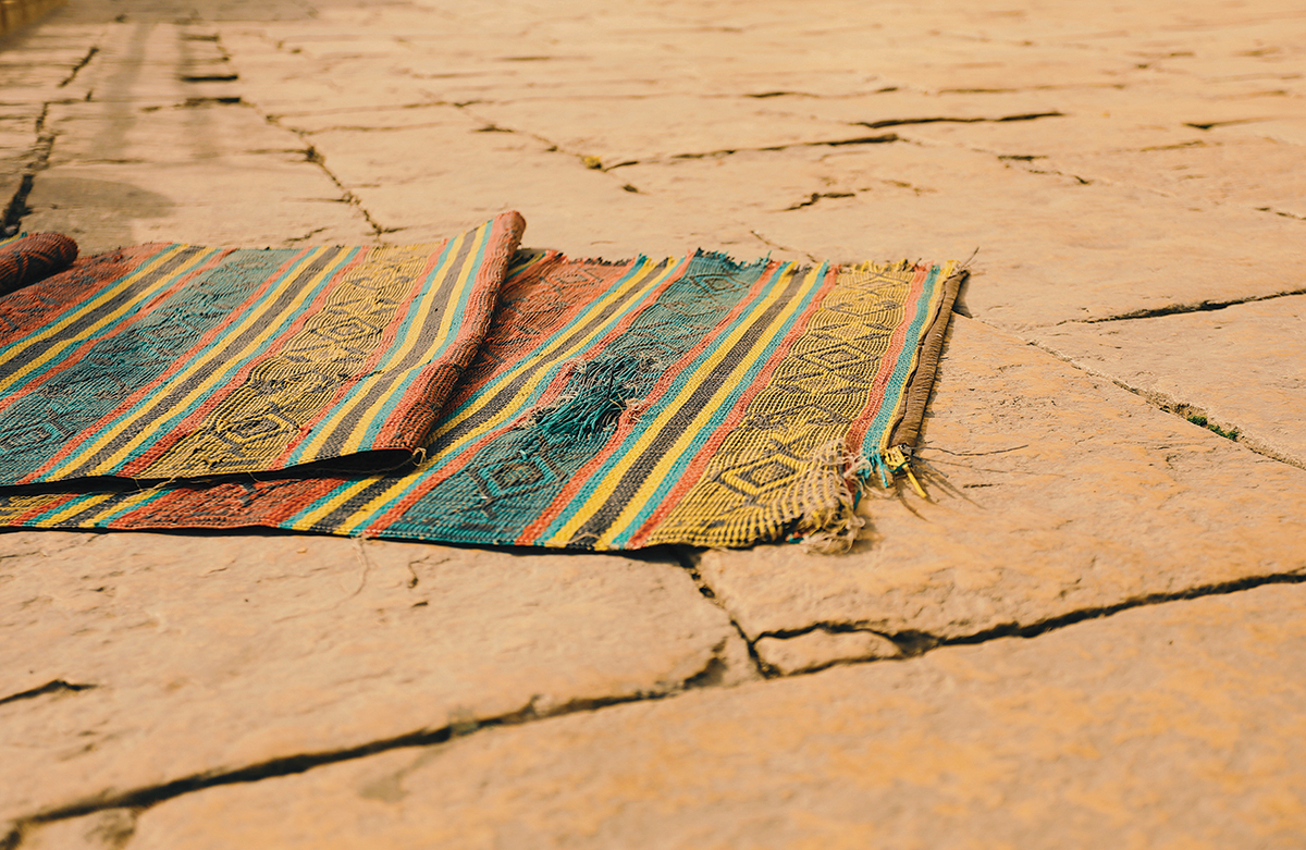 Colorful woven rug on rustic stone pathway outdoors in warm lighting.