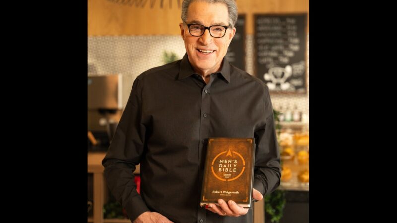 Man smiling, holding a copy of Men's Daily Bible in a cozy setting.