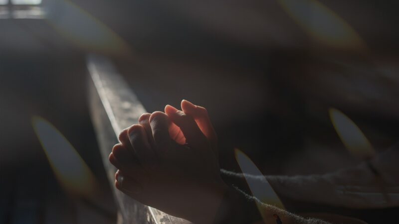 Hands clasped in prayer with candlelight, creating a peaceful, spiritual atmosphere.