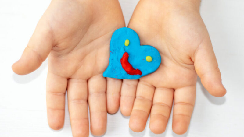 kid mother woman hands with red clay plasticine hearts shape in palm.many colored hearts on table blue yellow colour smiley face emoticon