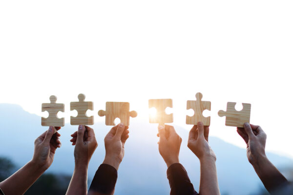 Teamwork and partnership concept. Hands are raised against a bright, white sky, each holding a piece of a wooden jigsaw puzzle. teamwork, problem solving, Charity, volunteer. Unity, team business.