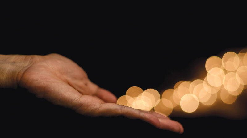 The hand releases yellow round shape bokeh light on black background.