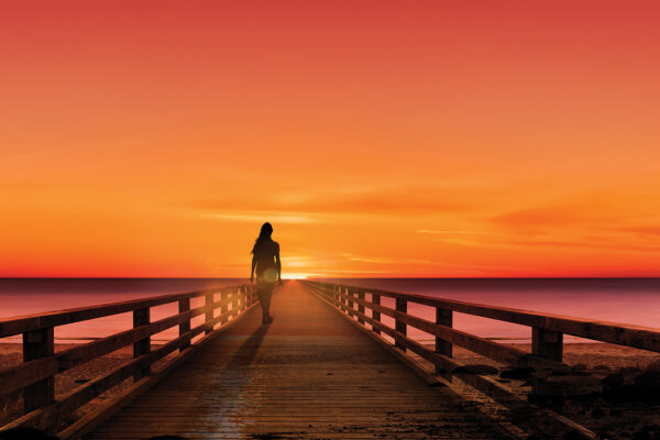 Silhouette of a woman on a jetty at sunset by the sea