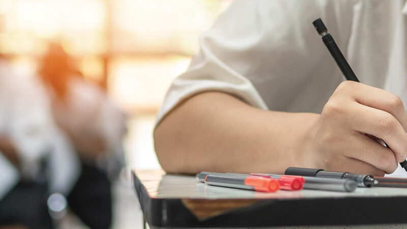 Exam at school with student's taking educational admission test in class, thinking hard, writing answer in university classroom, education and world literacy day concept